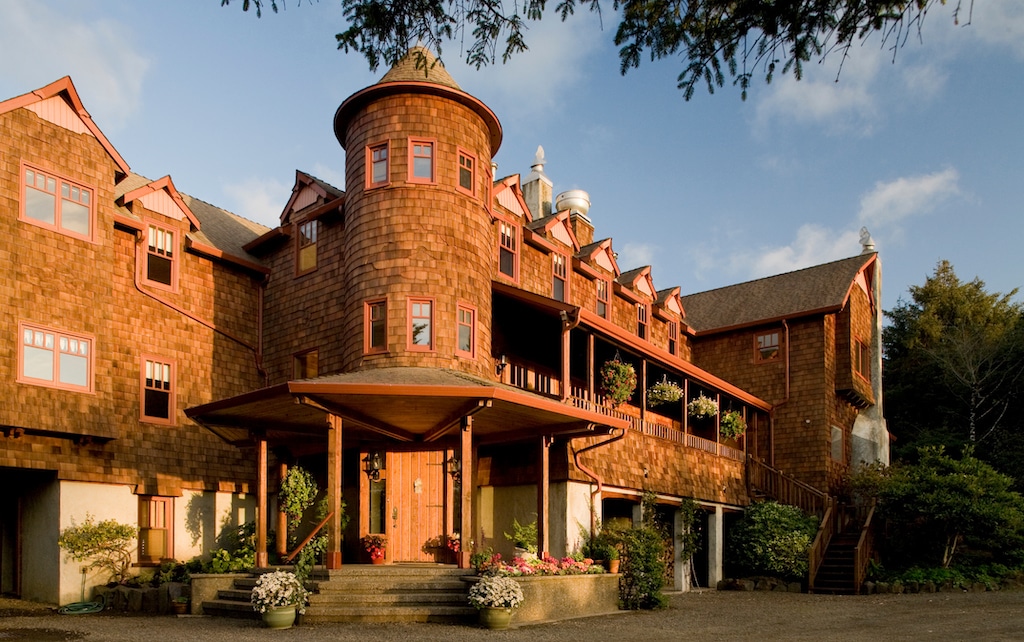 A multi-story shingled building with a central turret and covered entrance, set against a clear blue sky.