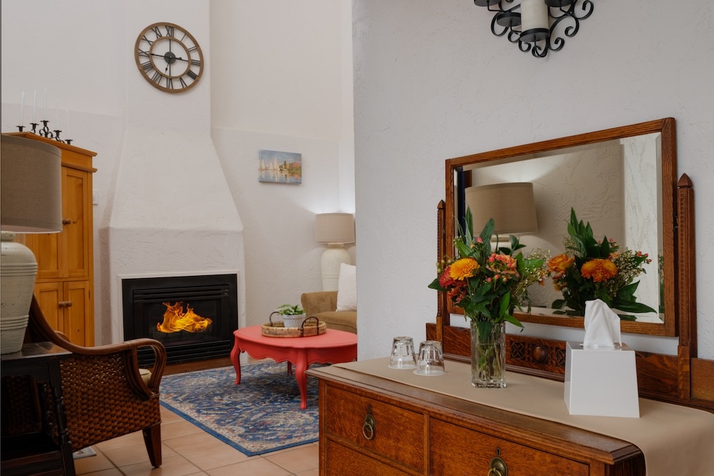 A living room interior featuring a fireplace, a red coffee table, and a wooden dresser with a mirror and flowers.