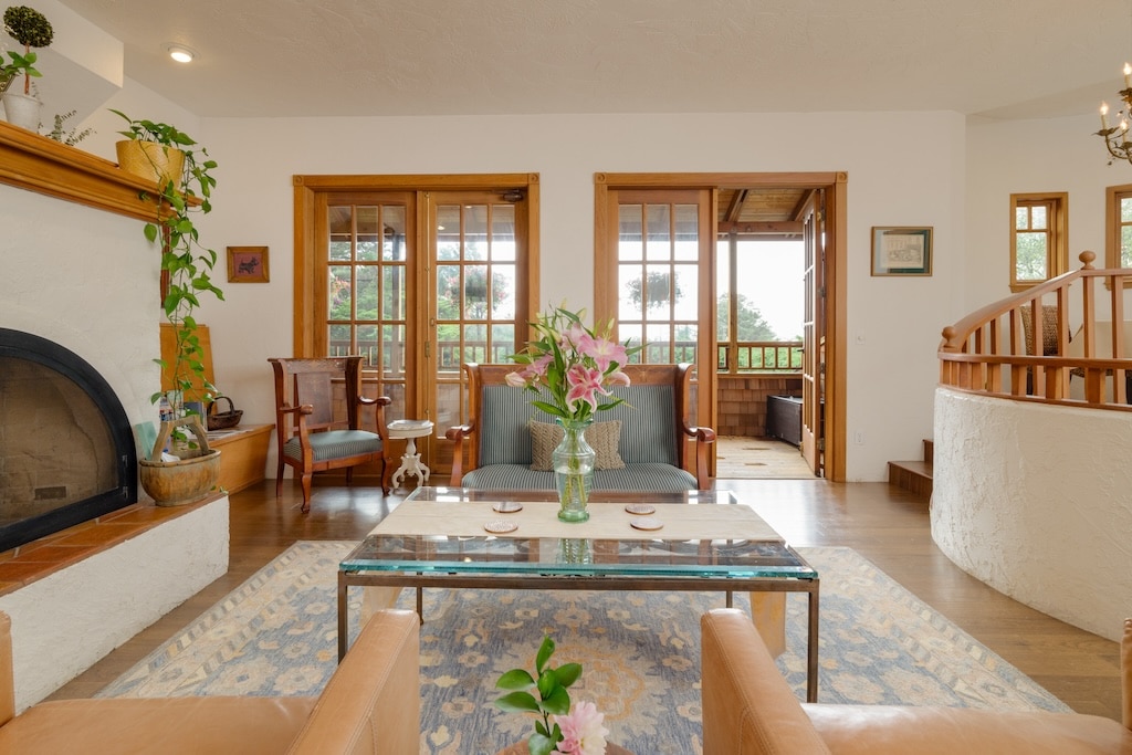 A bright, airy living room with a fireplace, seating area, glass coffee table, and an open balcony doorway.