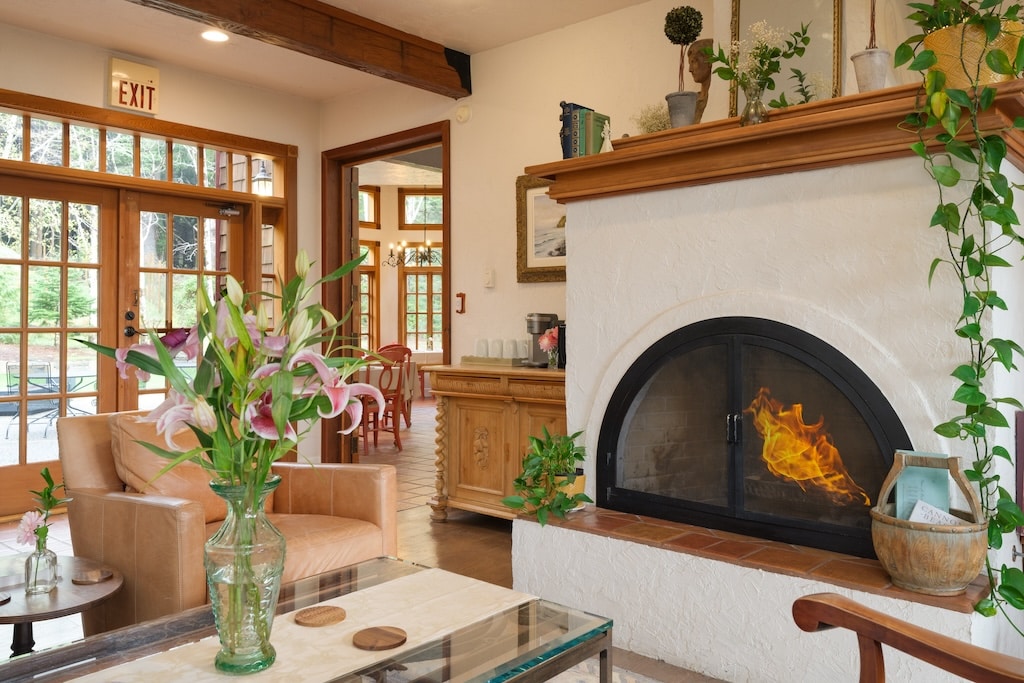 A living room features a lit fireplace, comfortable chairs, a coffee table with flowers, and an arched doorway.