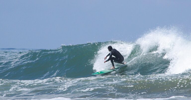 A surfer in a wetsuit rides a breaking wave on a sunny day.