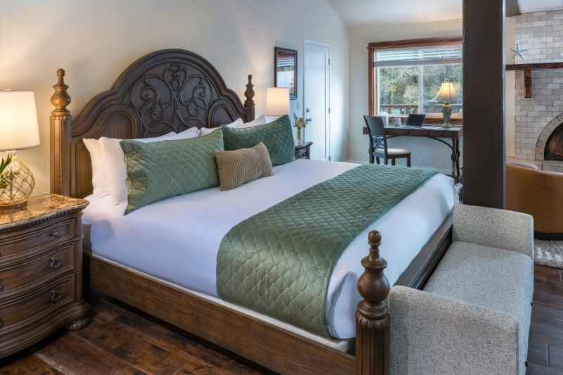 A hotel room with a large bed, wooden nightstand, desk area, and stone fireplace.