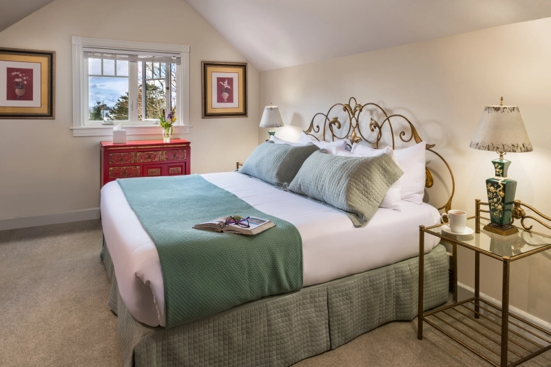 A cozy bedroom with a bed featuring a green runner, a red dresser, and a nightstand with a lamp.