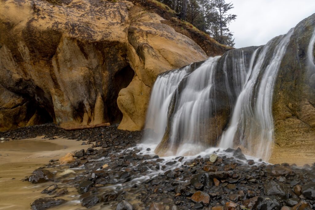 Waterfall of Fall Creek runs into beach on stormy day at Hug Point state park